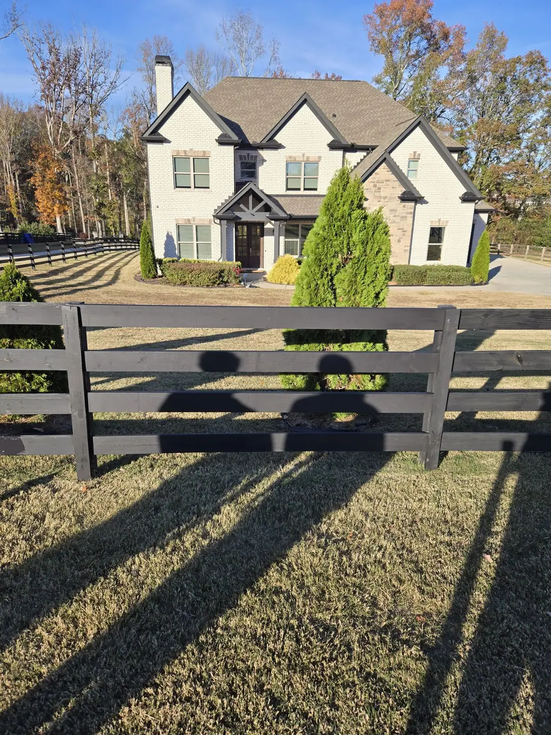After: the same black four-board farm fence repaired, rails straight in front of the house